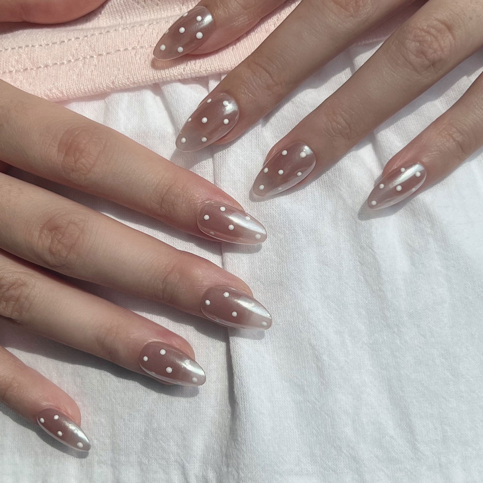 Close-up of hands with almond-shaped nails featuring a clear coat and white polka dot design on a white background. LuxeCharm