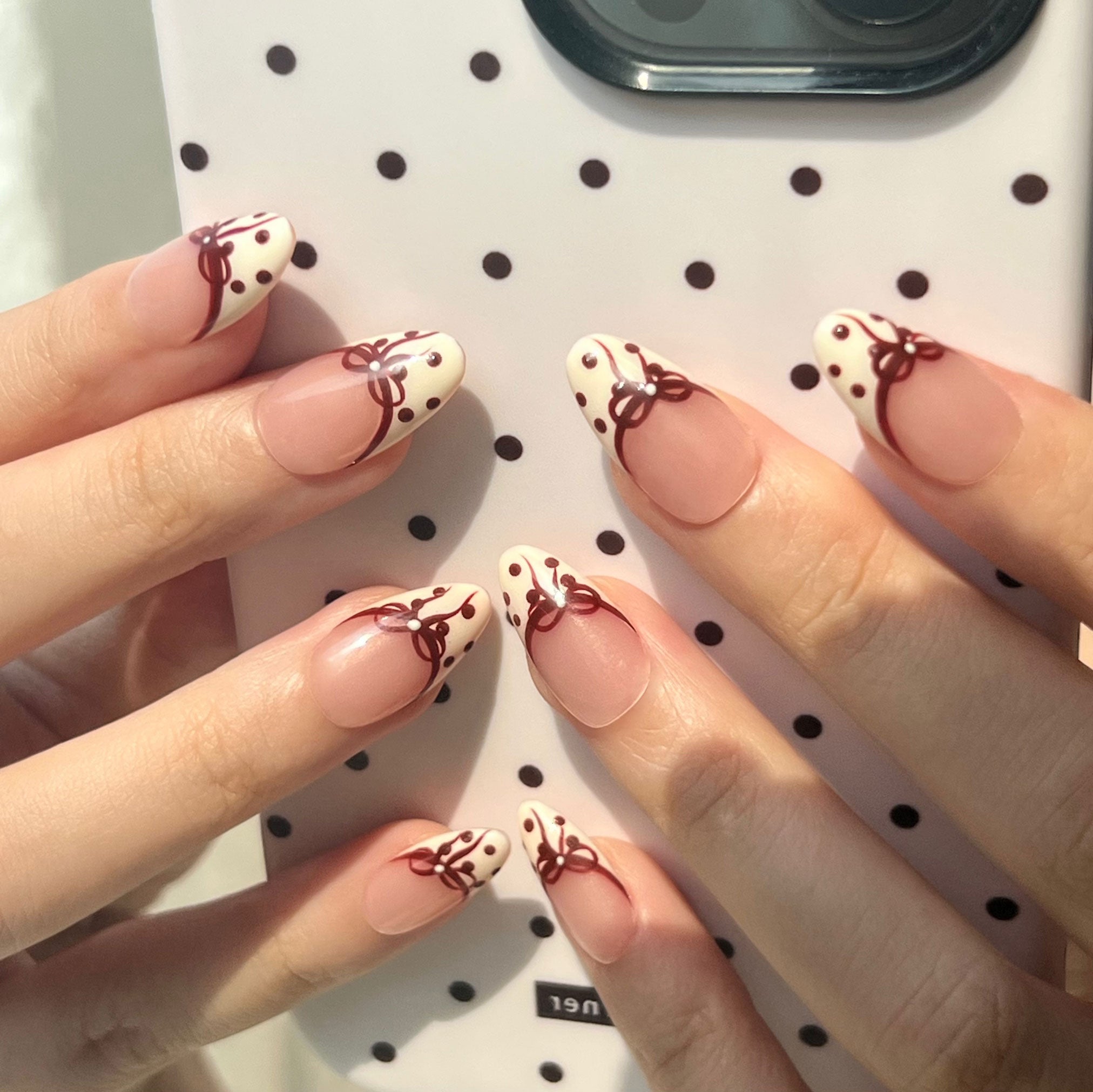 Nails with decorative red bows and polka dots on a polka dot iphone case background. LuxeCharm press on nails