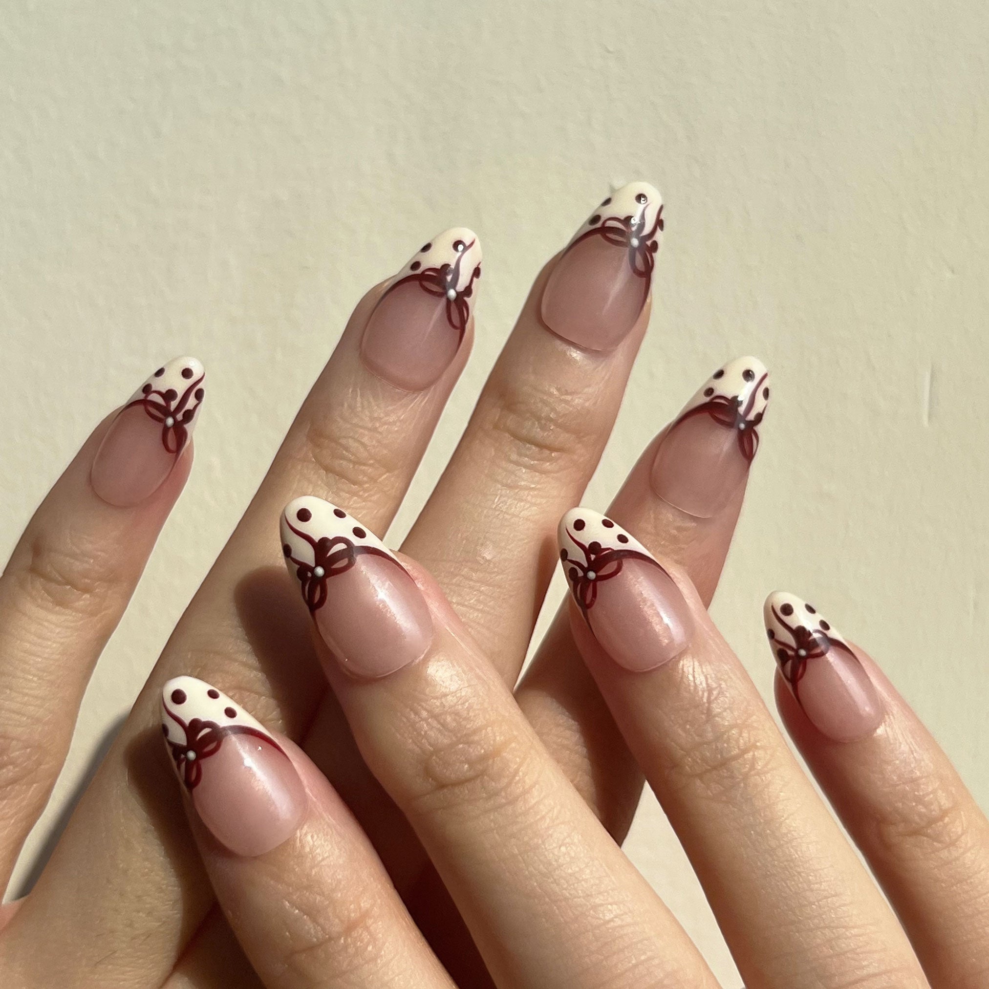 Nails with red bow and polka dots design on a neutral background. On-hand display. LuxeCharm press on nails