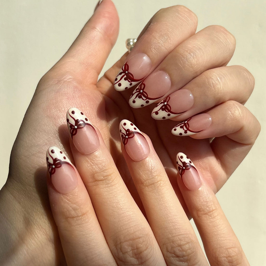 Hand with fake nails featuring polka dots and red bows on a neutral background. LuxeCharm press on nails