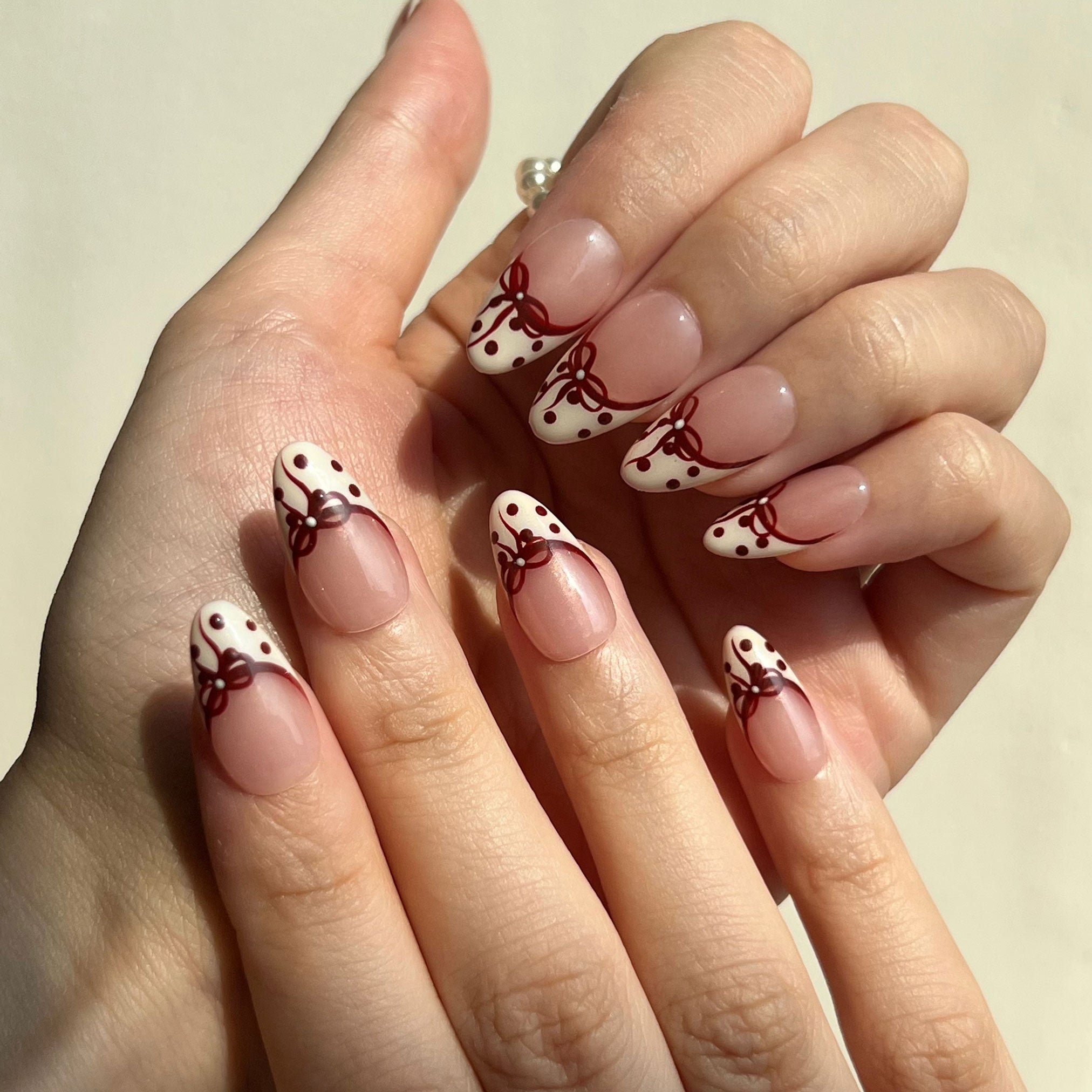 Hand with fake nails featuring polka dots and red bows on a neutral background. LuxeCharm press on nails