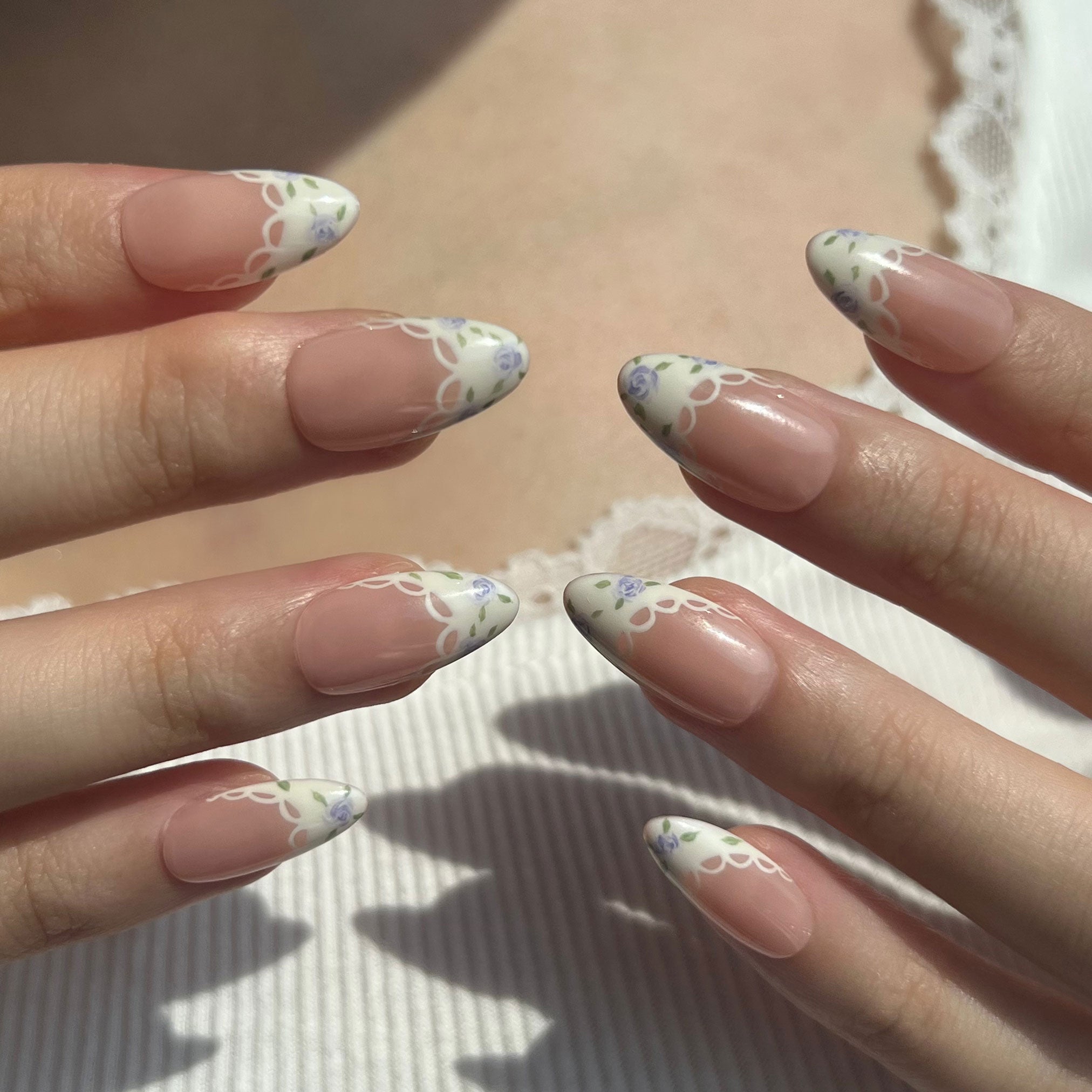 Close-up of hands with floral nail design on a neutral background. Set of purple coquette nail art designs with hand-painted purple floral patterns. LuxeCharm press on nails
