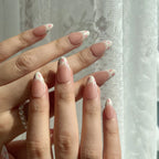 Close-up of a hand with pink fake nails and floral designs against a light background. Set of coquette nail art designs with hand-painted pink floral patterns