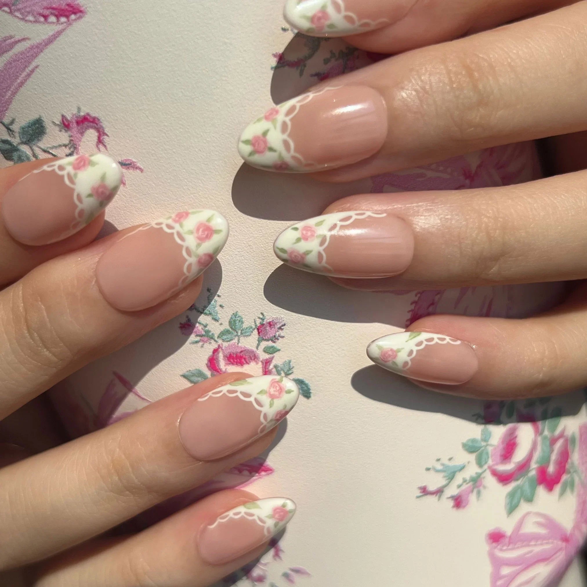 Close-up of hands with floral nail design on a floral background. Set of coquette nail art designs with hand-painted pink floral patterns