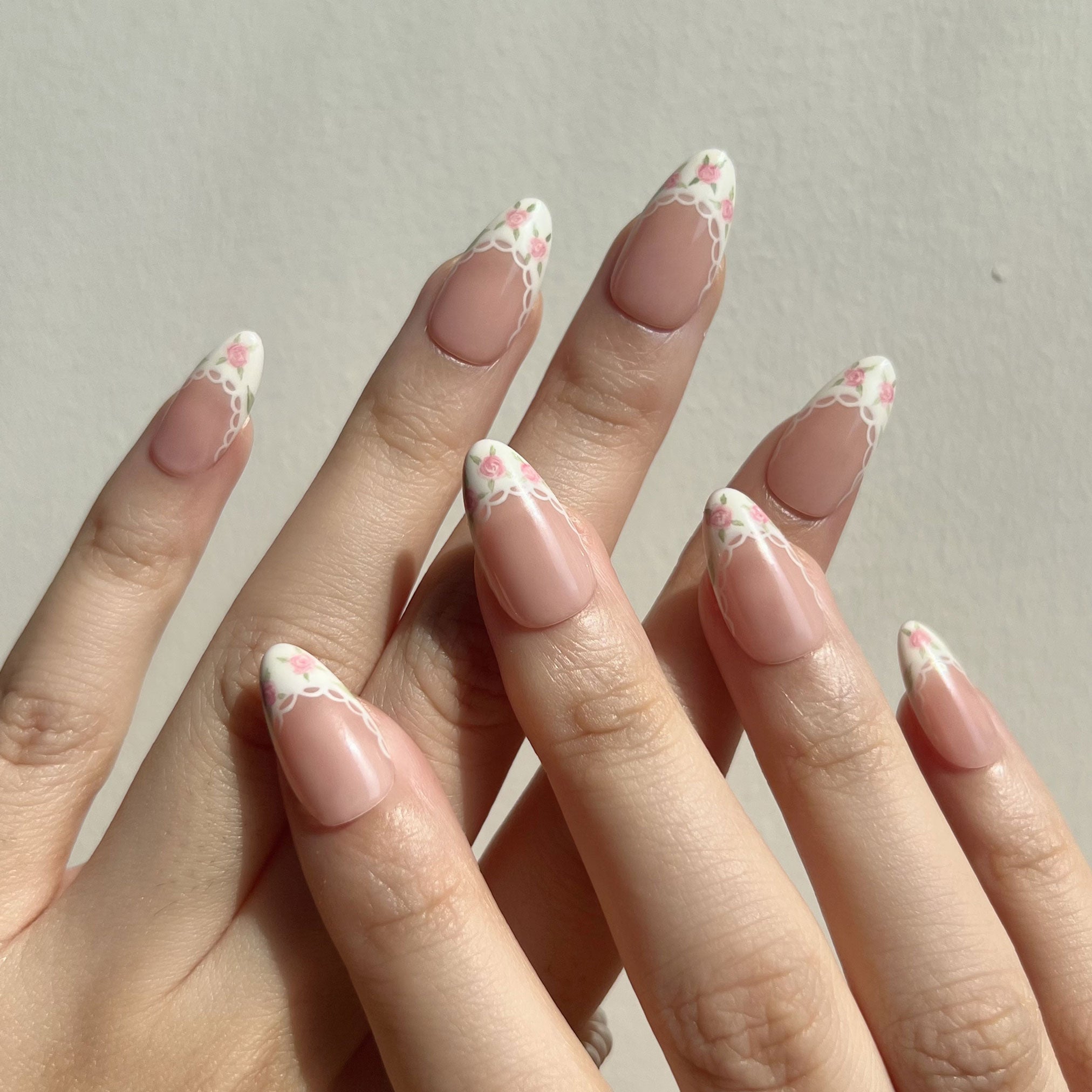 Fake nails on hand with a floral design on a neutral background. Set of coquette nail art designs with hand-painted pink floral patterns