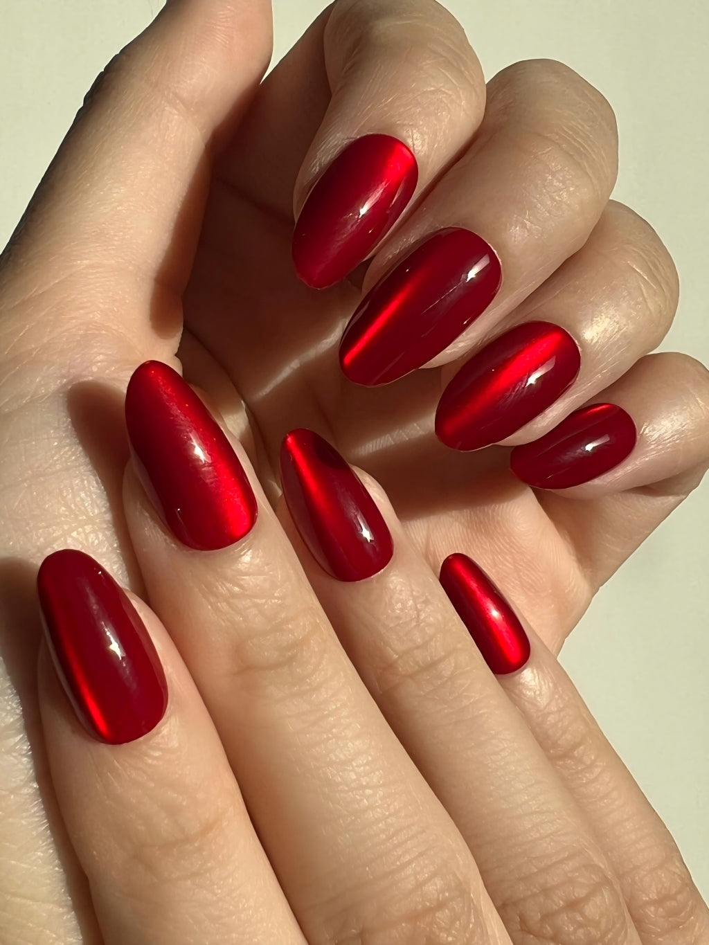 Hands with LuxeCharm Ruby Marble Cat-Eye Short Almond Nails on a neutral background