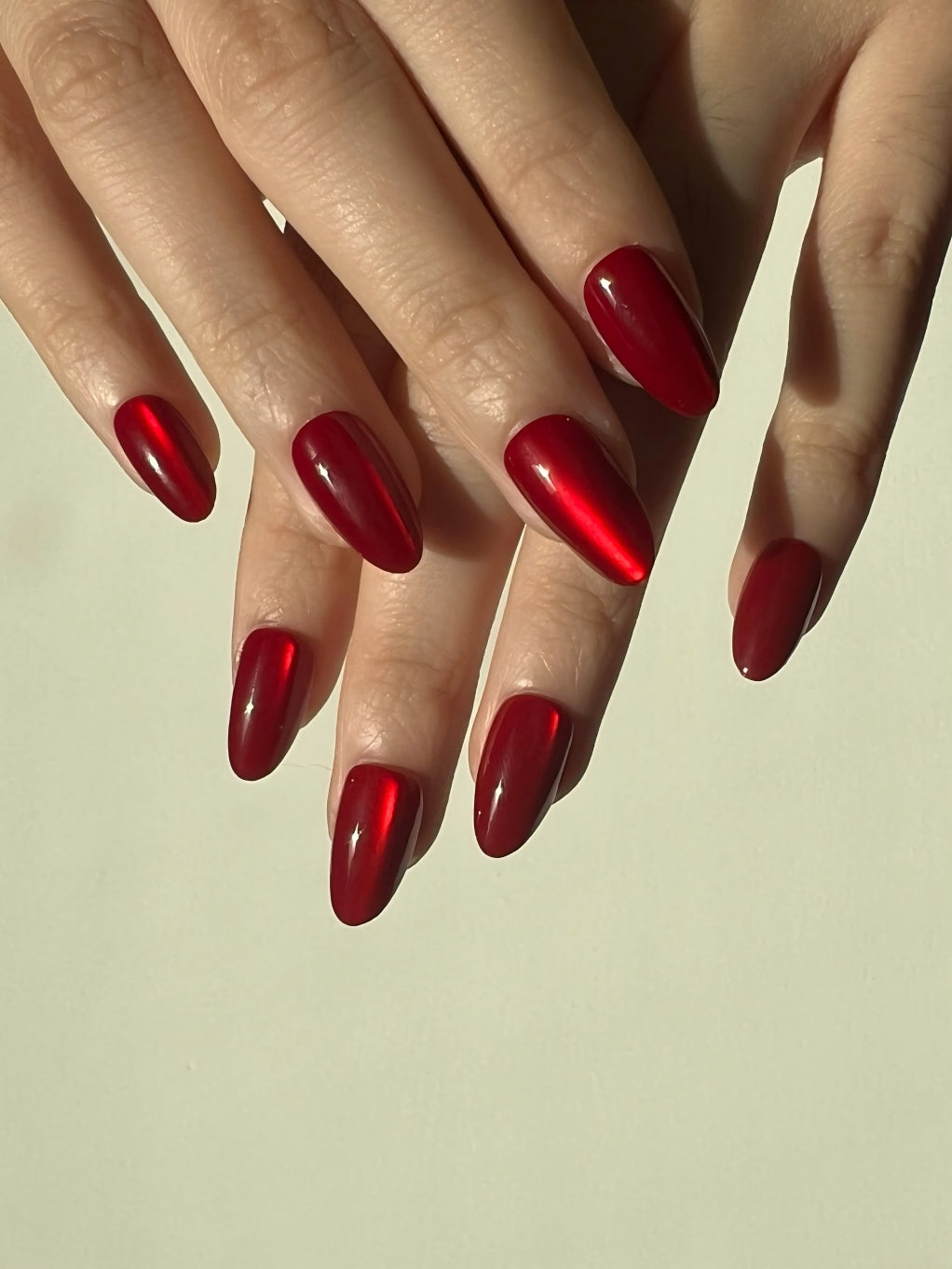 Close-up of hands with LuxeCharm Ruby Marble Cat-Eye Short Almond Nails on a beige background