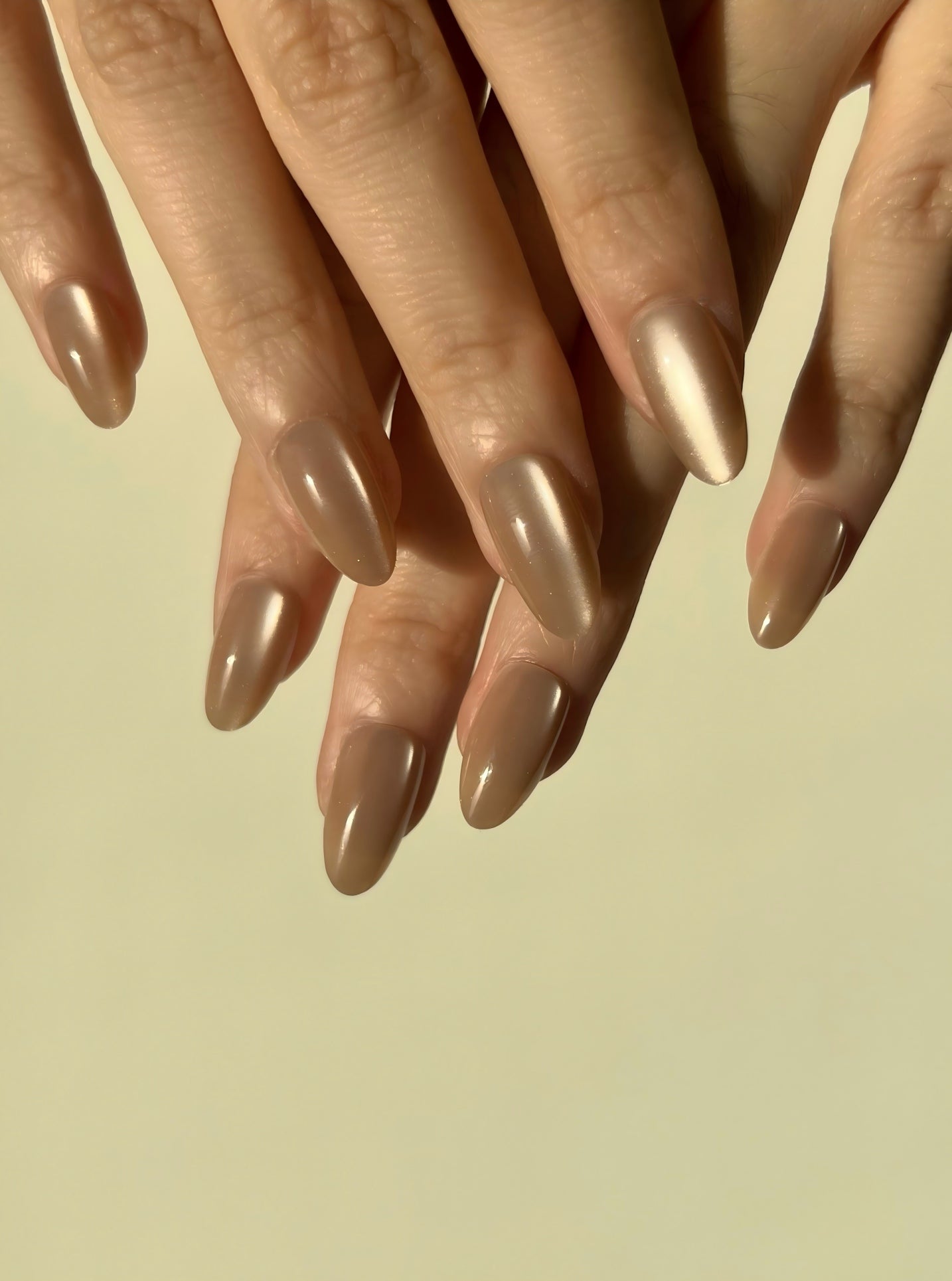 Close-up of hands with LuxeCharm Sandstone Glow Cat-Eye Short Almond Nails on a beige background