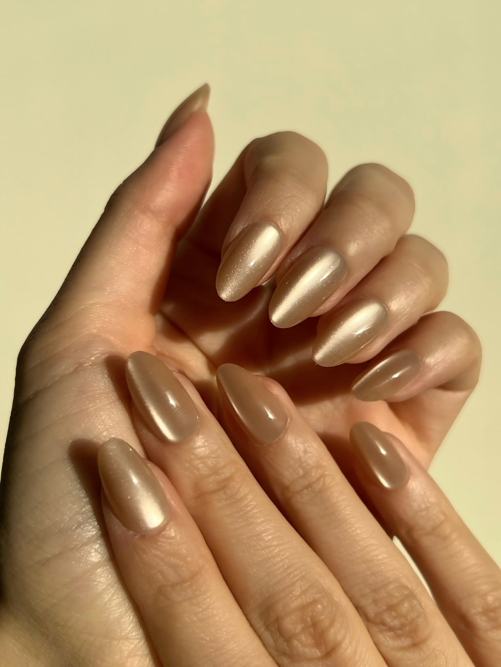 Close-up of a hand with LuxeCharm Sandstone Glow Cat-Eye Short Almond Nails on a plain background