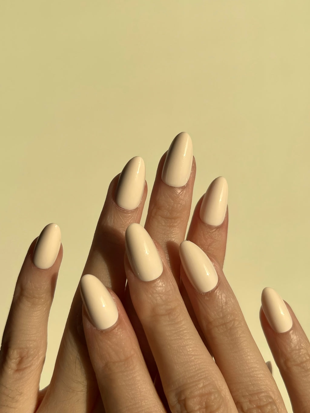 Close-up of a hand with LuxeCharm Soft Cream press on nails on a yellow background