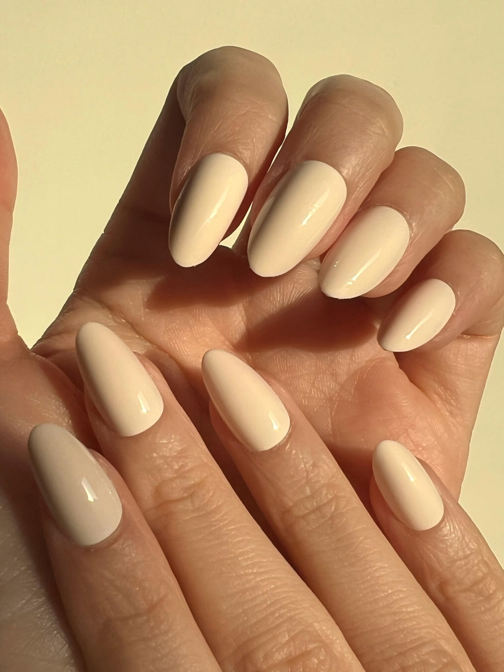 Hand with LuxeCharm Soft Cream press on nails on a light yellow background