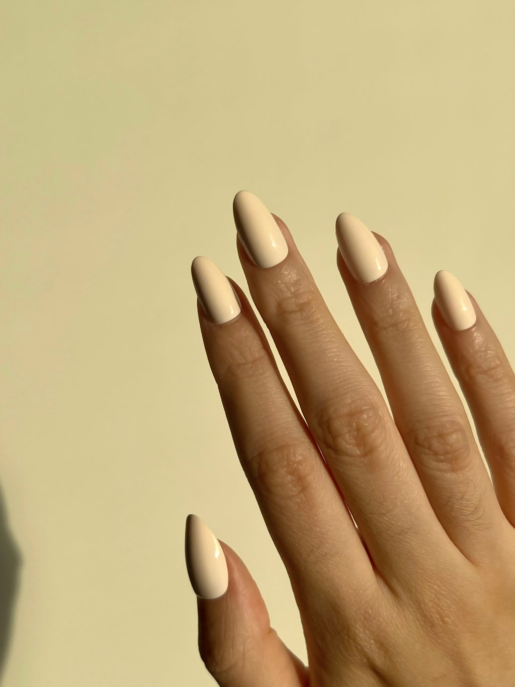 Hand with LuxeCharm Soft Cream press on nails on a beige background