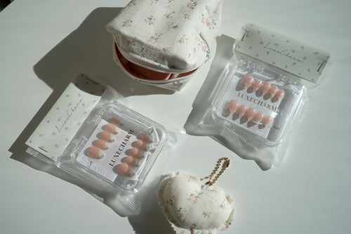 LuxeCharm Bloom & Carry Bundle including a handmade carry pouch, a handmade charm, and 2 petal whisper press on nails sets on a white surface with floral-patterned boxes.