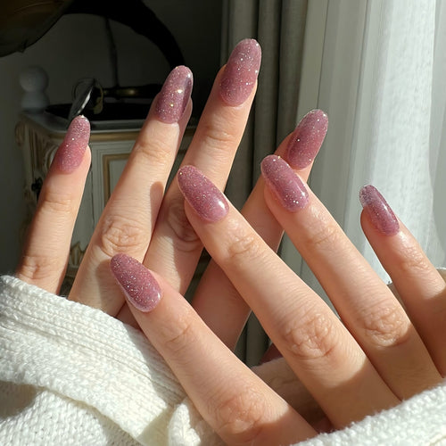 Close-up of hands with pink glitter nails against a neutral background. LuxeCharm press on nails