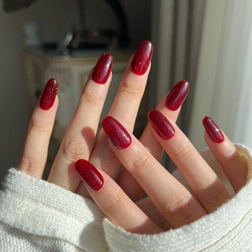 Close-up of a hand with red glitter nails  against a neutral background