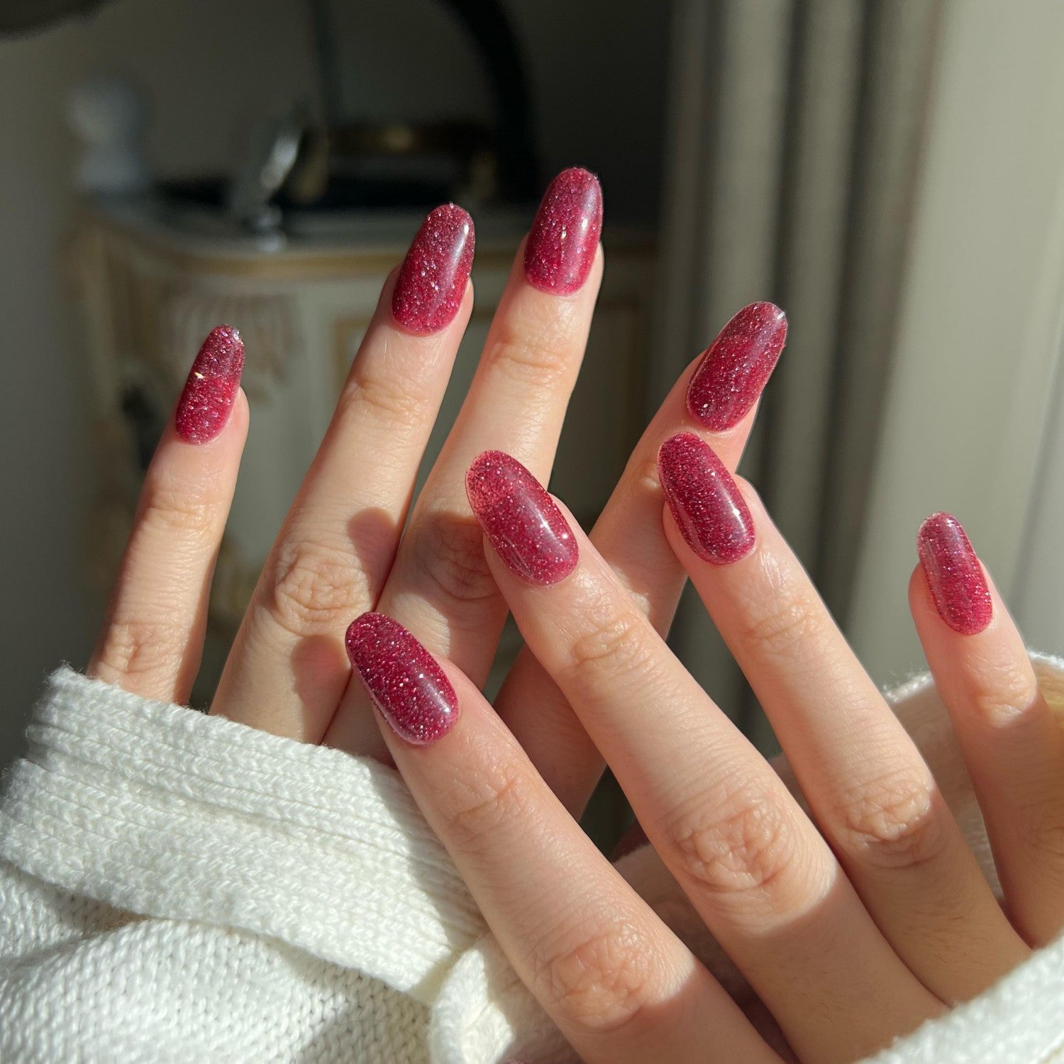 Close-up of a hand with dark pink glitter nails against a neutral background