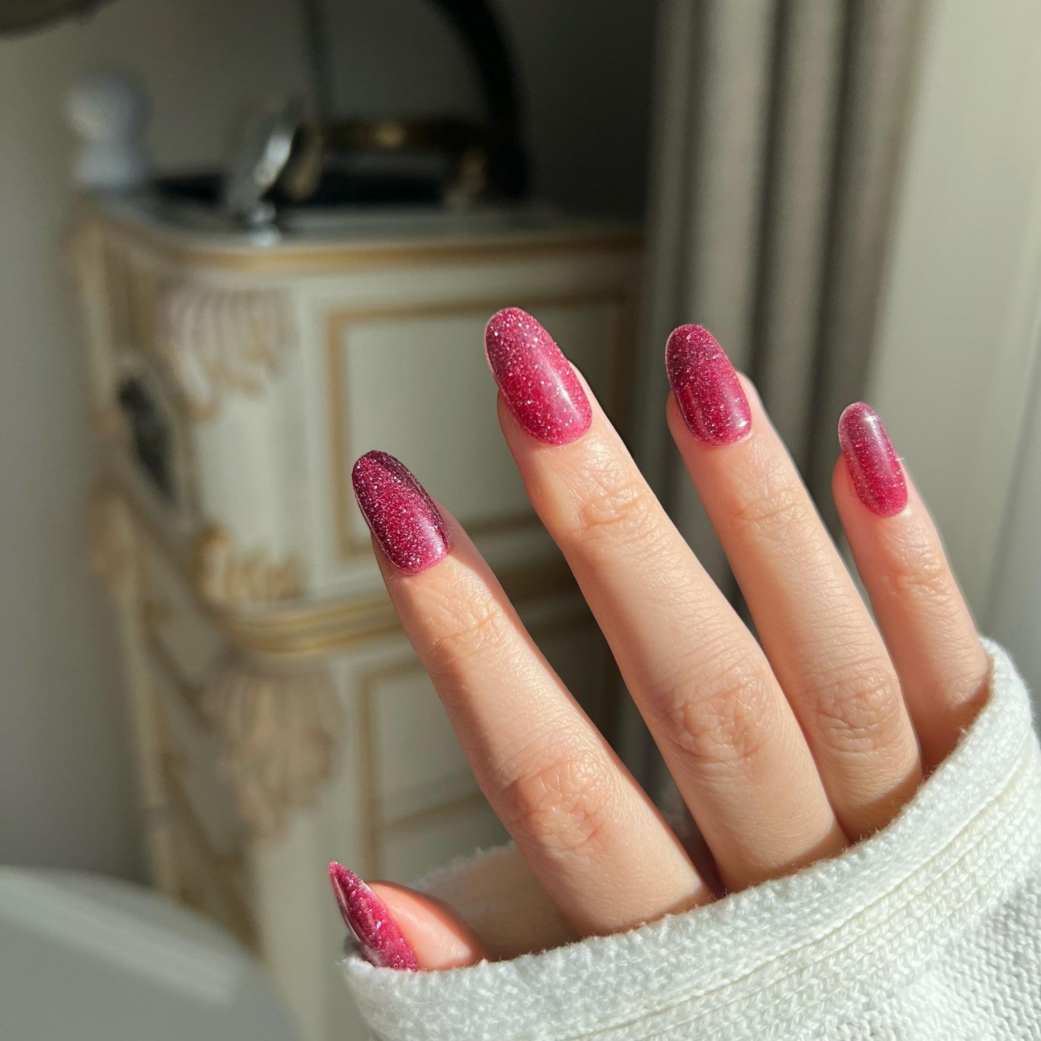 Close-up of a hand with dark pink glitter nail in a blurred indoor setting