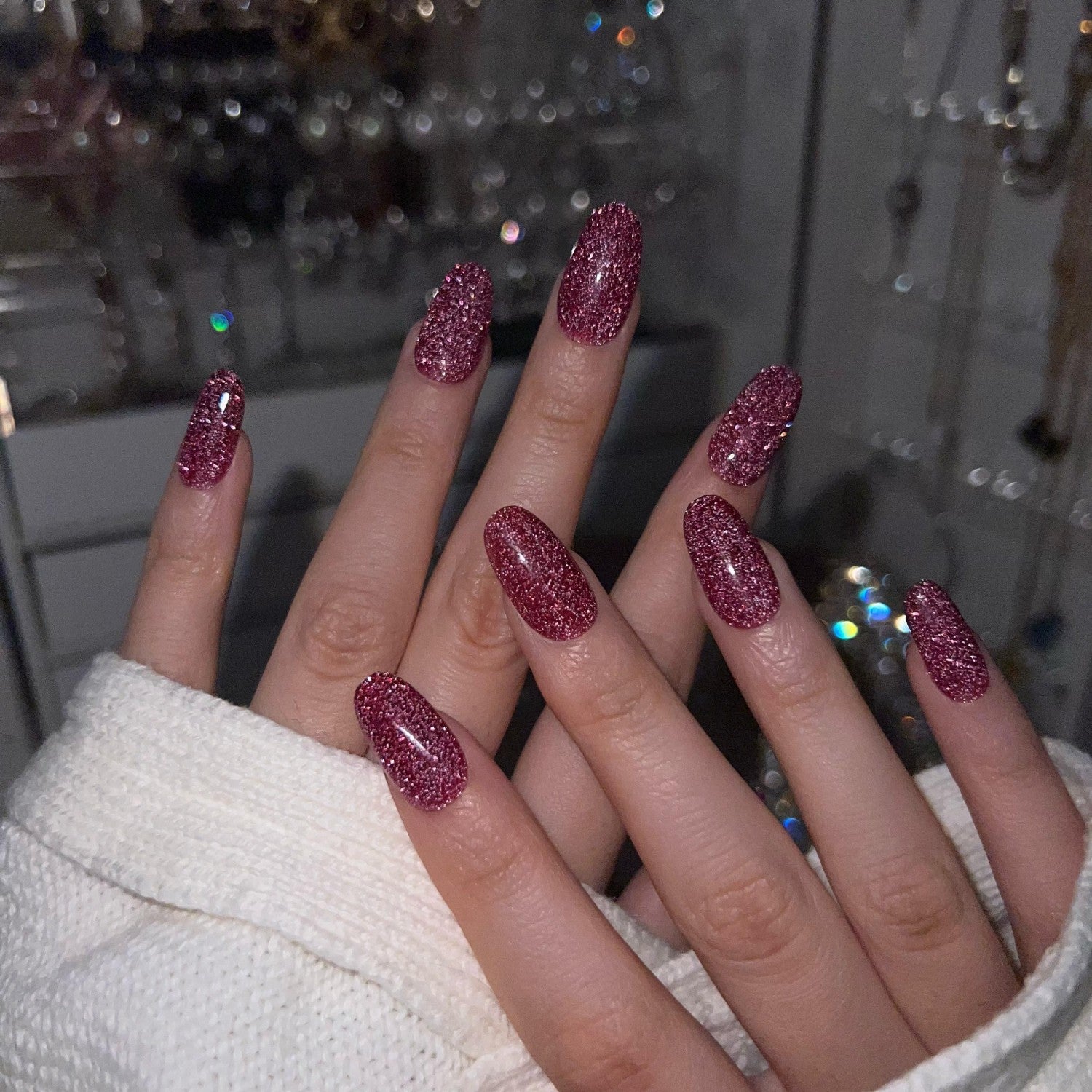 Hand with dark pink glitter nails against a blurred background