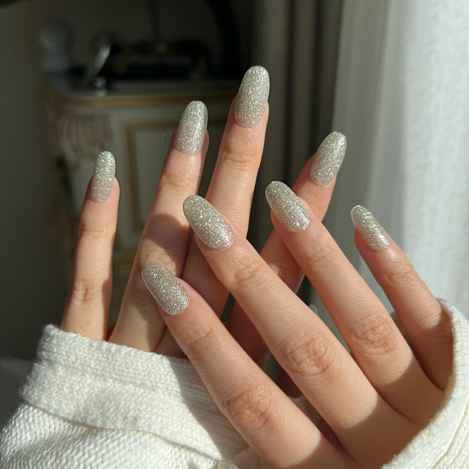 Close-up of a hand with silver glitter nails against a neutral background