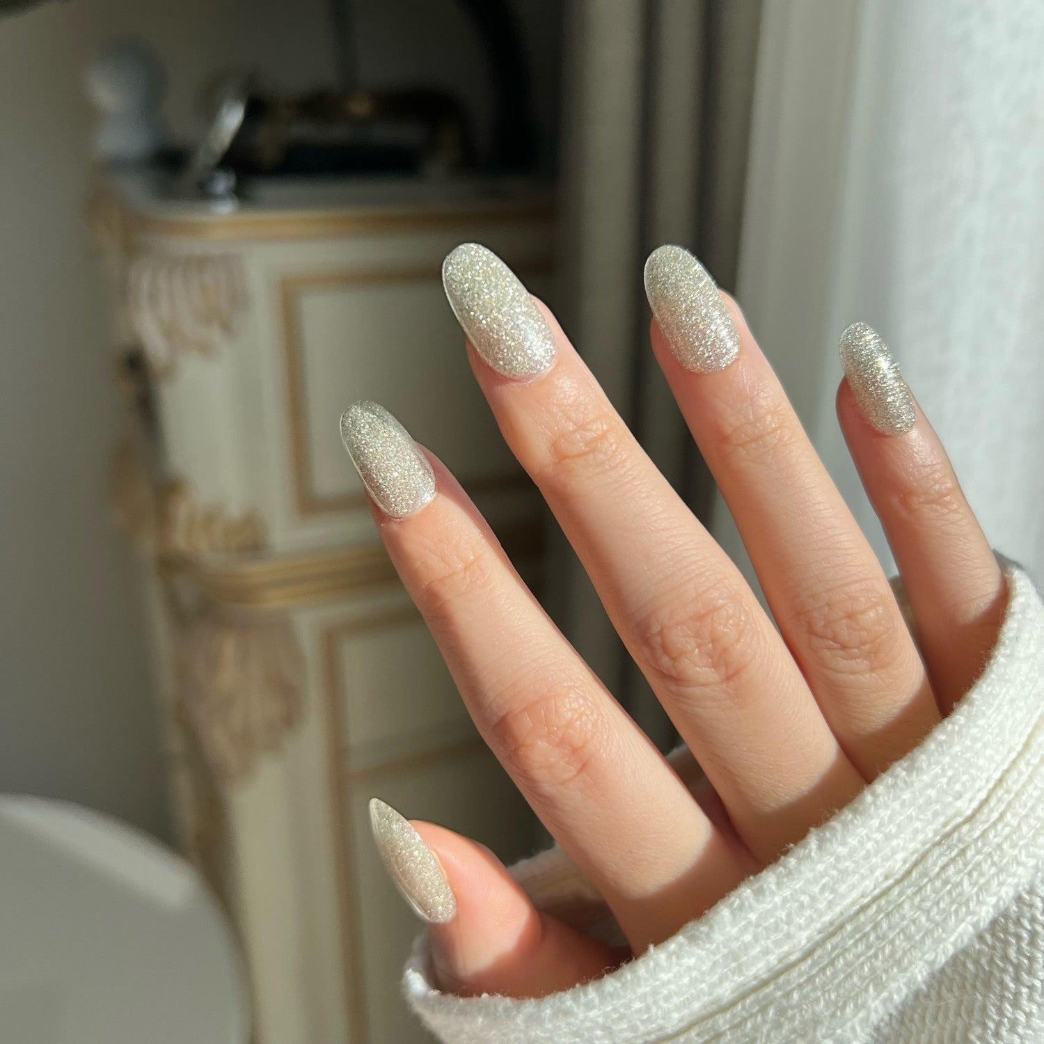 Hand with silver glittery nail in a blurred indoor setting