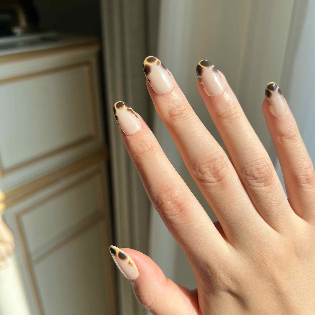 Hand model wearing LuxeCharm Glazed Amber press-on nails with nude base and tortoiseshell detailing