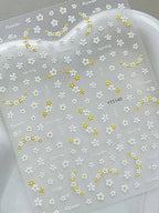 Sheet of white and yellow floral nail art stickers on a clear background. LuxeCharm nail stickers