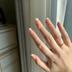 Hand with  LuxeTip French extra short square nails in light brown color and a gold ring against a neutral background