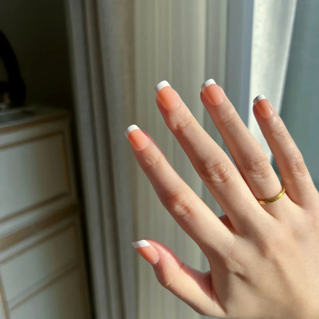 Hand with  LuxeTip French extra short square nails in light brown color and a gold ring against a neutral background