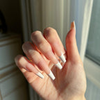 Hand with LuxeTip French long coffin press on nails in peach color against a neutral background