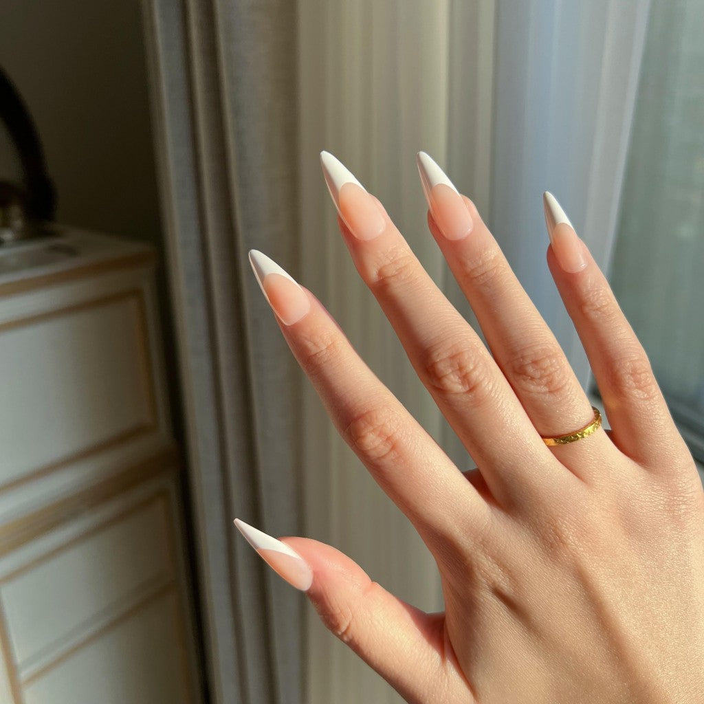 Hand with LuxeTip French long stiletto press on nails in peach color, wearing a gold ring, against a neutral background.