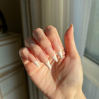 Hand with  LuxeTip French long stiletto press on nails in peach color against a neutral background