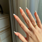 Hand with  LuxeTip French medium almond press-on nails in light brown colo ragainst a neutral background