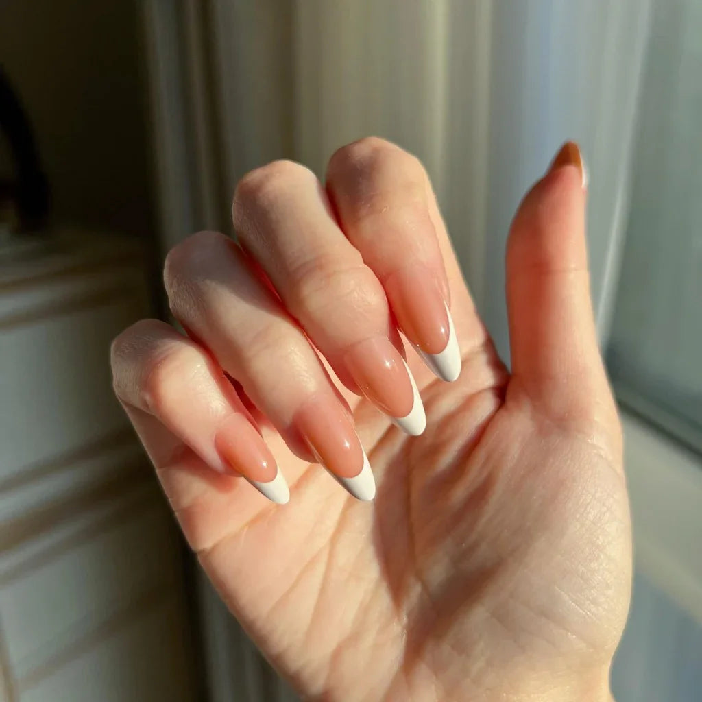 Hand with LuxeTip French medium almond press-on nails in light brown color, held against a neutral background.