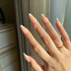 Hand with  LuxeTip French medium almond press-on nails in peach color and a gold ring on a neutral background