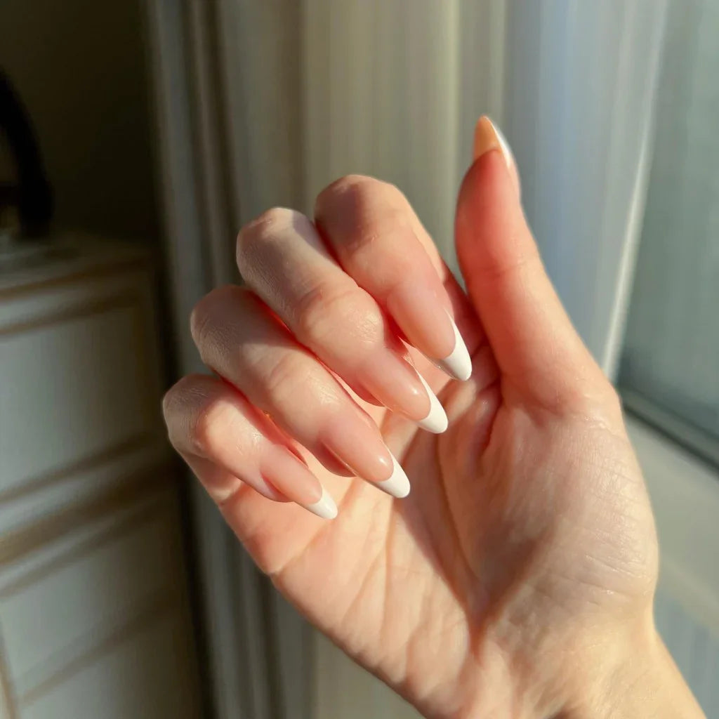 Hand with LuxeTip French medium almond press-on nails in peach color in front of a window with light streaming in.