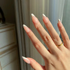 Hand with LuxeTip French medium almond press-on nails in pink color, painted white, wearing a gold ring, against a neutral background.