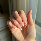 Hand with LuxeTip French medium almond press-on nails in pink color holding a small object against a neutral background