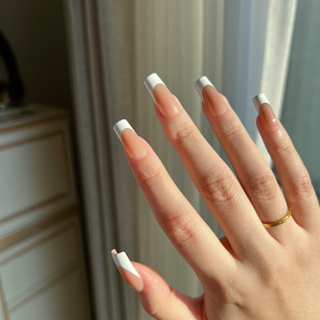 Hand with  LuxeTip French medium square press on nails in mocha color, wearing a gold ring, against a neutral background.