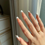 Hand with  LuxeTip French medium square press on nails in mocha color, wearing a gold ring, against a neutral background.