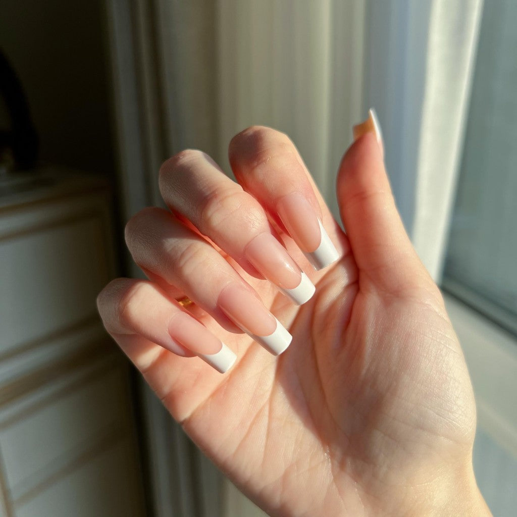 Hand with LuxeTip French medium square press on nails in peach color, in front of a window.