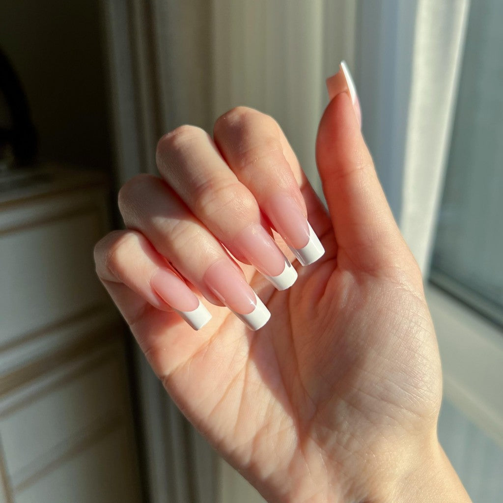 Hand with  LuxeTip French medium square press on nails in pink color, in front of a window