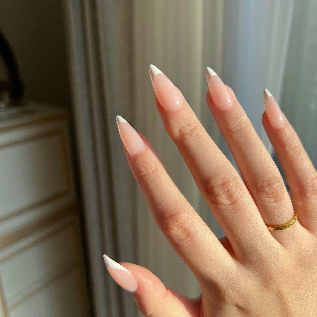 Hand with LuxeTip French medium stiletto press on nails in pink color and a gold ring against a neutral background