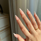 Hand with LuxeTip French medium stiletto press on nails in pink color and a gold ring against a neutral background