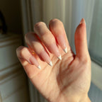 Hand withLuxeTip French medium stiletto press on nails in pink color against a blurred indoor background