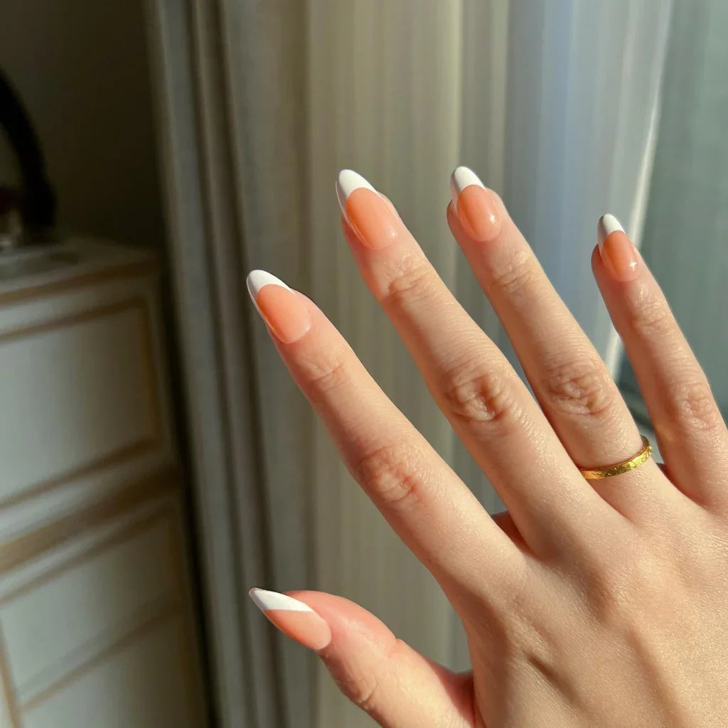 Hand with LuxeTip French short almond press on nails in light brown and a gold ring, blurred background