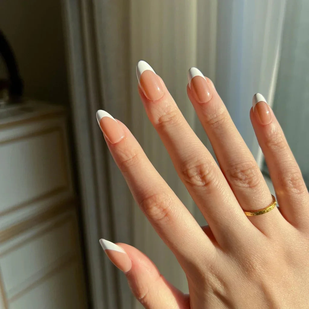 Hand with LuxeTip French short almond press on nails in mocha color and a gold ring against a neutral background