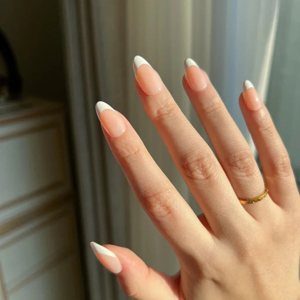 Hand with LuxeTip French short almond nails in peach color and a gold ring against a neutral background