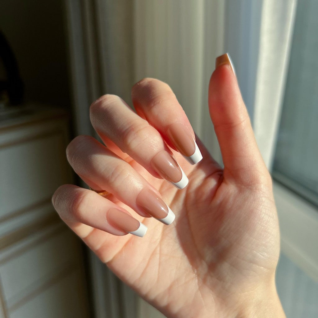 Hand with LuxeTip French short coffin press on nails in mocha color, in front of a window