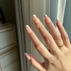 Hand with LuxeTip French short coffin press on nails in peach color, in a neutral color scheme against a blurred indoor background