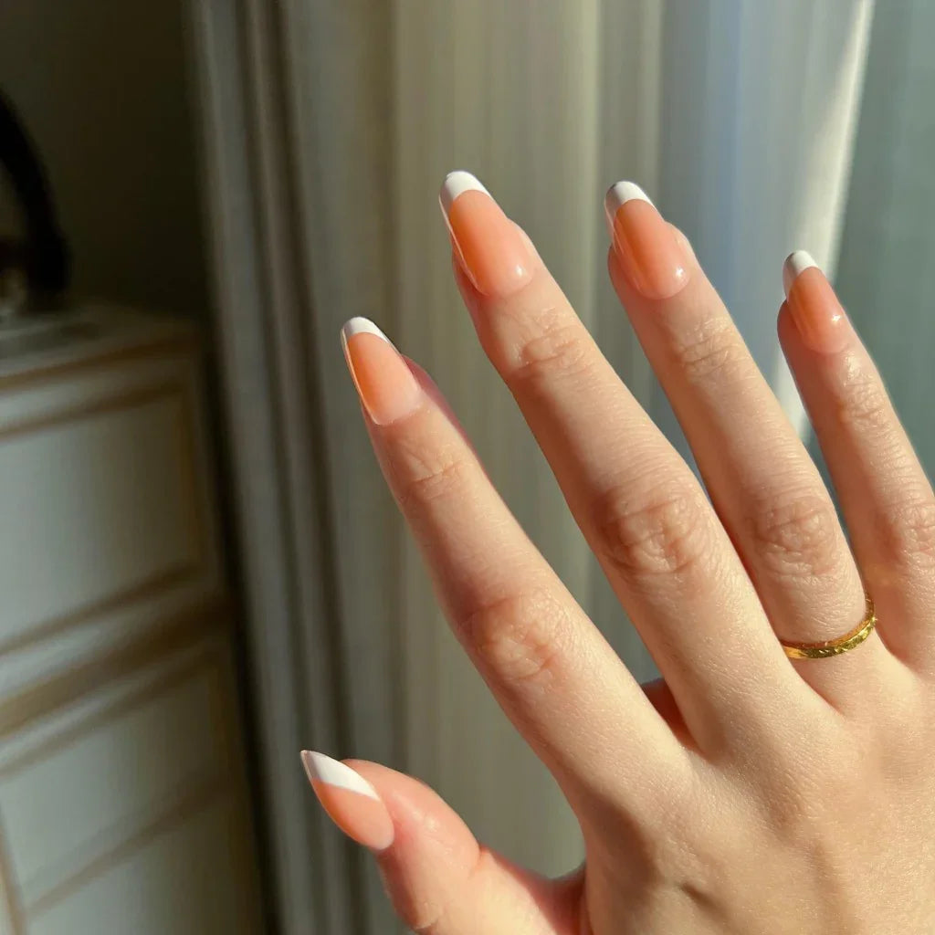 Close-up of a hand with LuxeTip French short oval nails in light brown against a neutral color scheme.